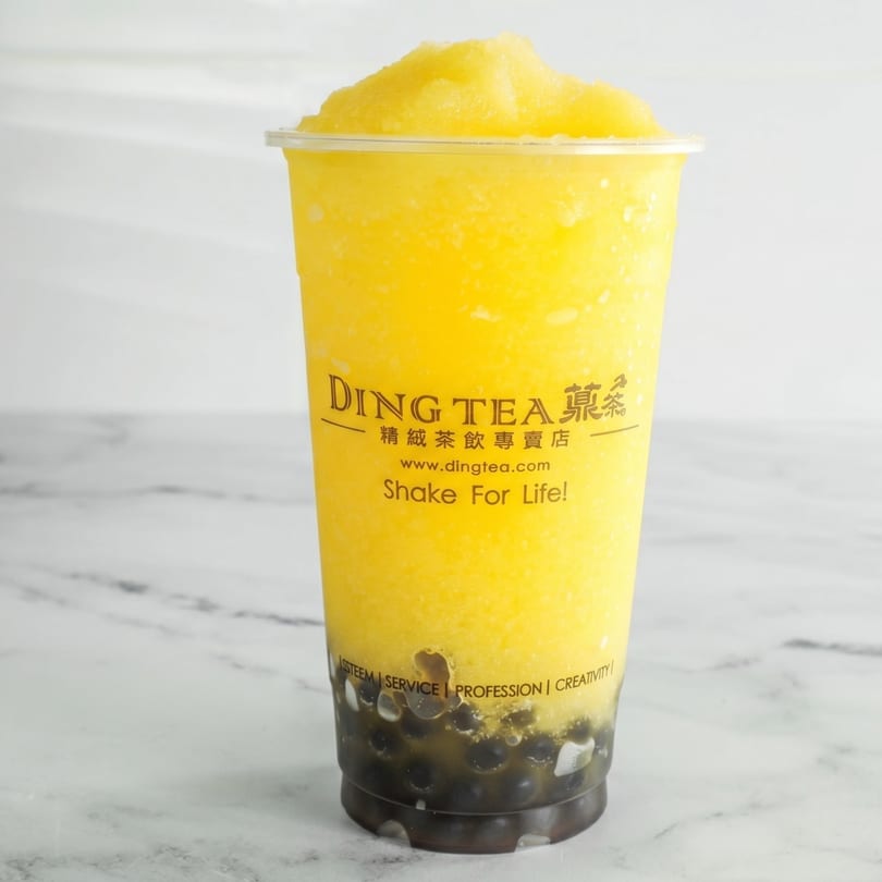 A Ding Tea mango slush with dark boba pearls at the bottom, on a white marble surface.