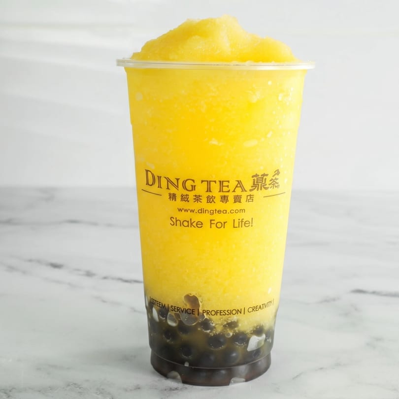 A Ding Tea mango slush with dark boba pearls at the bottom, on a white marble surface.
